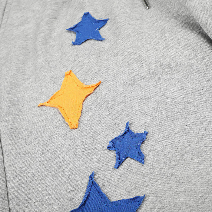 Close-up of blue and orange star appliqués arranged along the gray sweatpants leg