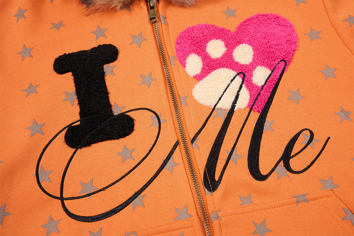 Orange hoodie chest close-up showing gray stars, front zipper, and textured I love Me graphic