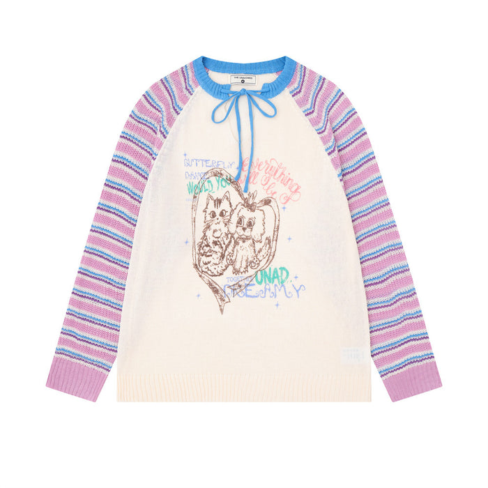 Front view of a cream knit pullover with pink and blue striped raglan sleeves, blue tie neck, and cat graphic