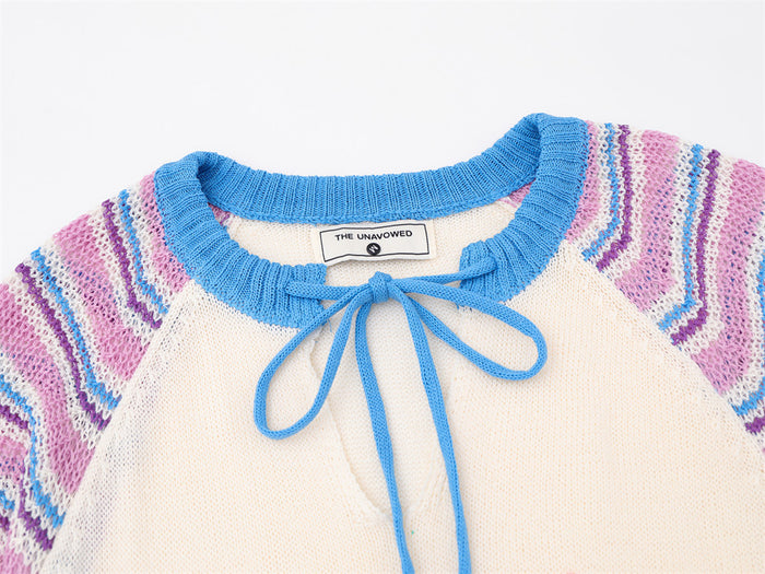 Close-up of the blue ribbed neckline and matching tie on a cream knit pullover