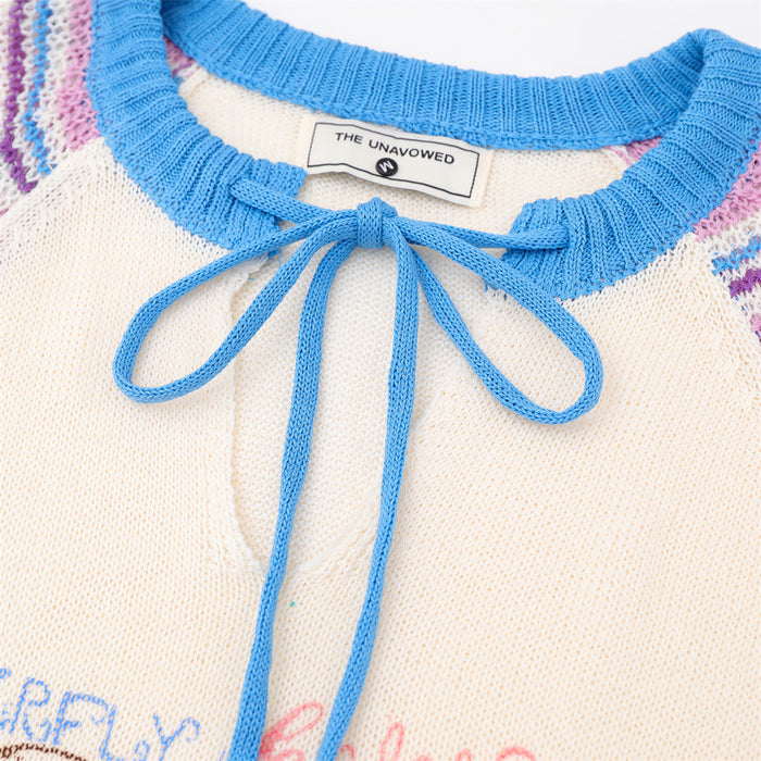 Detailed view of the blue knit tie bow, ribbed neckline, garment label, and cream sweater texture