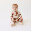 Baby wearing a brown and white patterned one piece on a white background