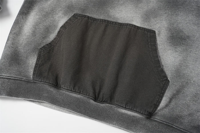 Close-up of the gray hoodie’s dark kangaroo pocket with visible stitching and ribbed lower hem