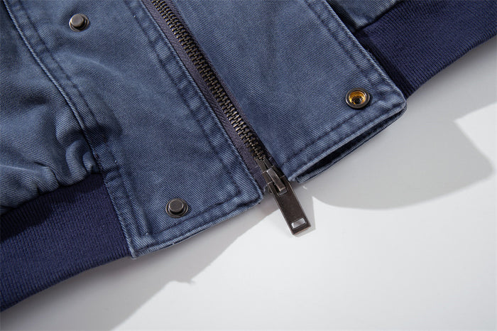 Close-up of the washed blue bomber jacket's front zipper, metal pull, snap buttons and dark ribbed hem