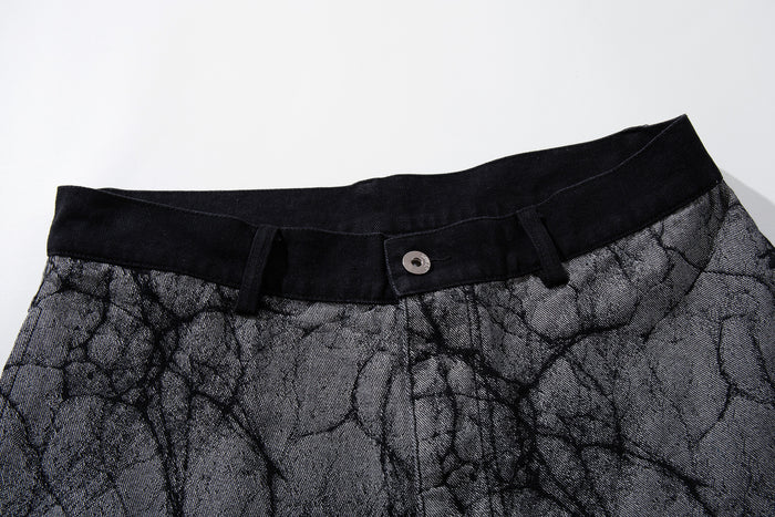 Close-up of the black waistband, belt loops, button, and gray crackle-print denim