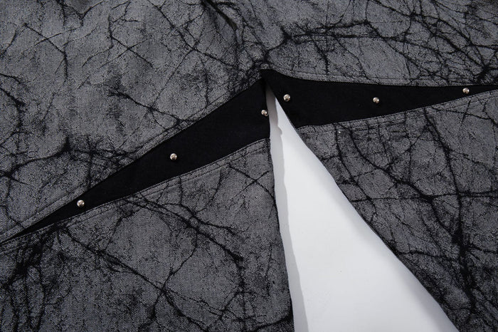 Close-up of a black diagonal stripe with small metal studs across gray crackle-print jeans