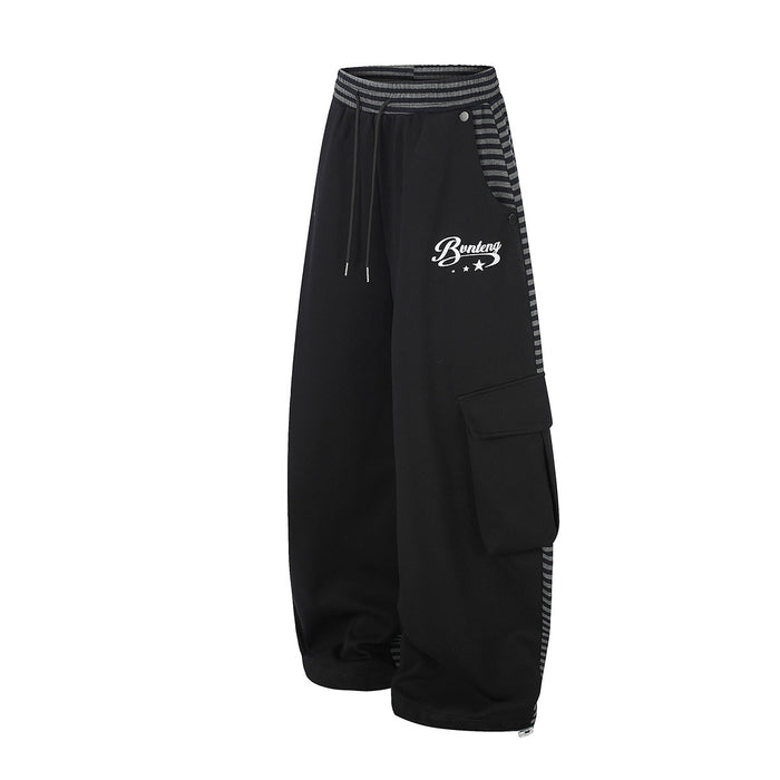 Side view of black wide-leg cargo pants showing a flap pocket, striped waistband panel and white script logo