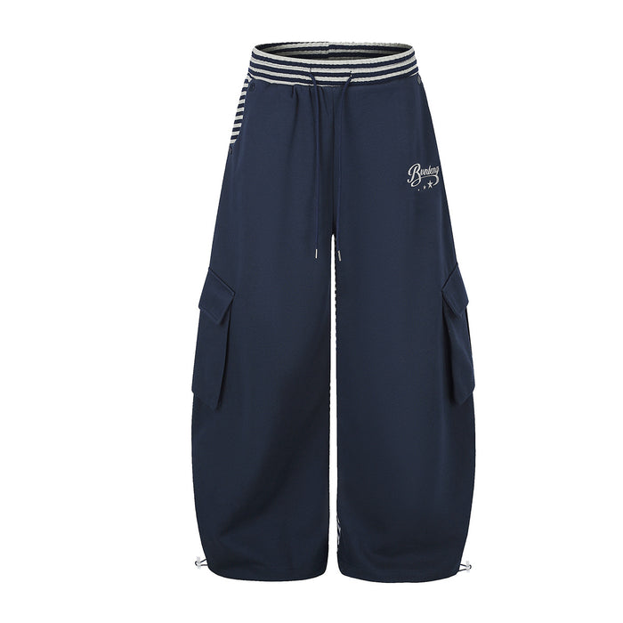 Front view of navy wide-leg cargo sweatpants with striped waistband, drawcord, side pockets and white script logo