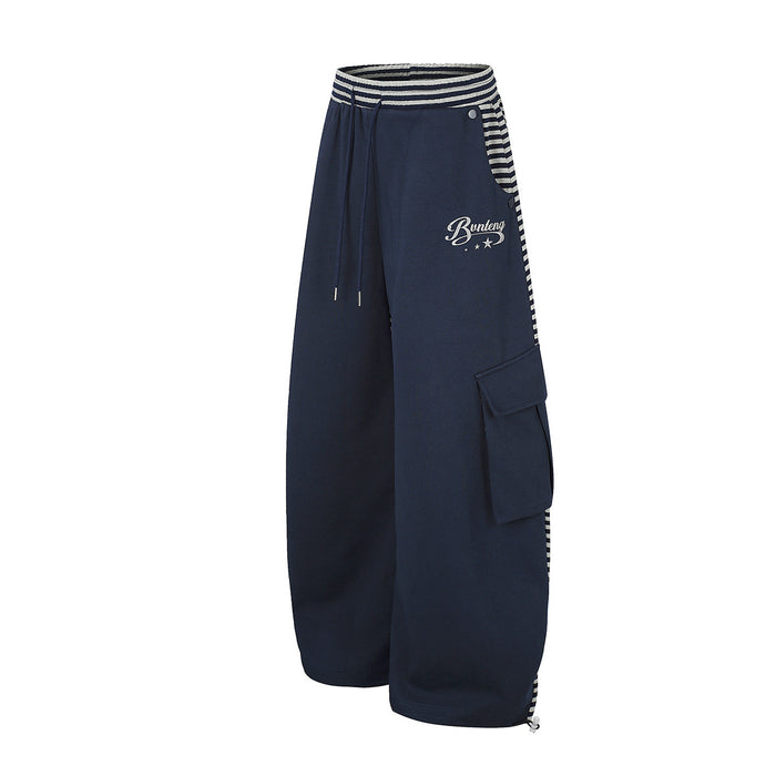 Side view of navy wide-leg cargo pants showing a flap pocket, striped waistband panel and white script logo