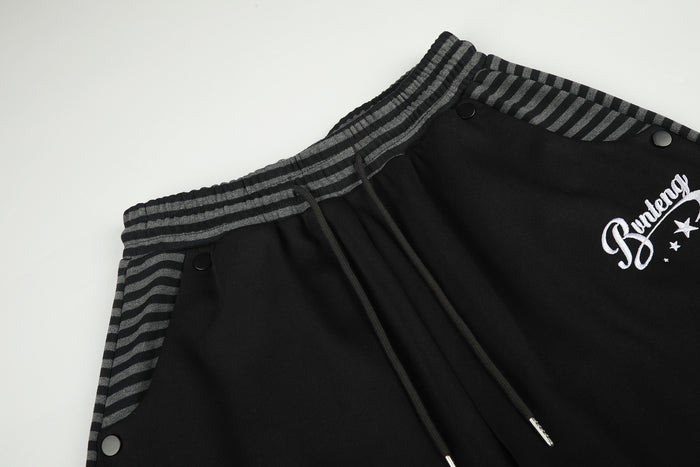 Close-up of black pants showing striped waistband, drawcord, snap pocket and white script logo