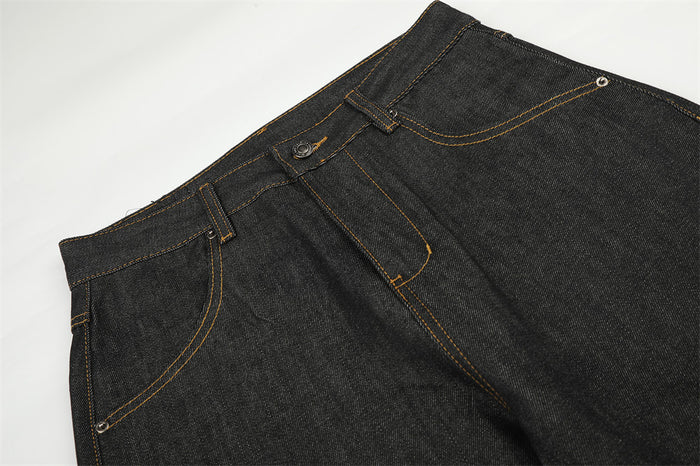 Close-up of the black jeans waistband and front pockets with contrasting orange stitching and metal rivets