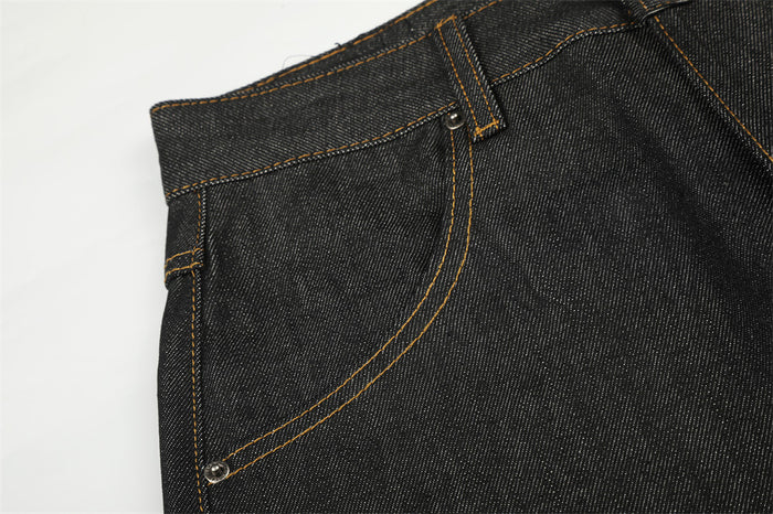 Close-up of a black denim front pocket with curved orange stitching, rivets, and belt loop