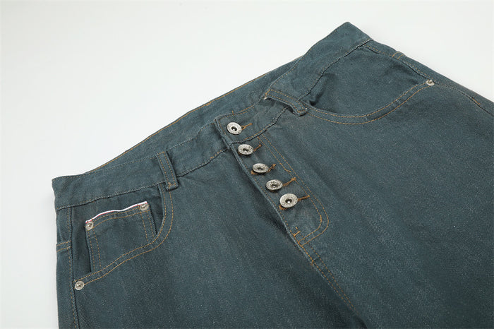 Close-up of the teal green jeans waistband showing the button fly, front pockets, belt loops, and contrast stitching