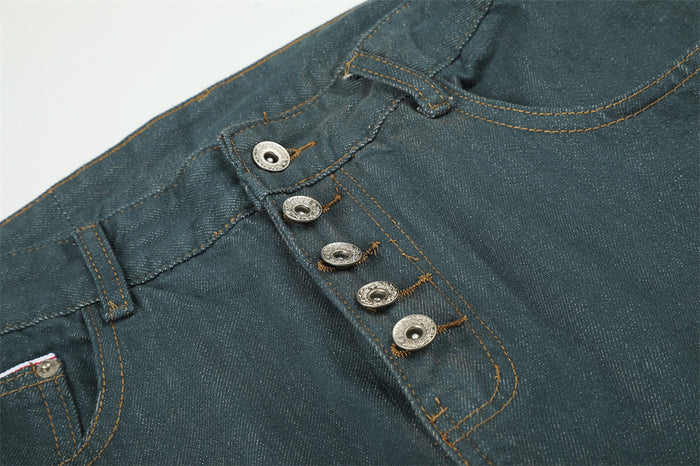 Detailed view of the teal green jeans button fly with four metal buttons and orange contrast stitching