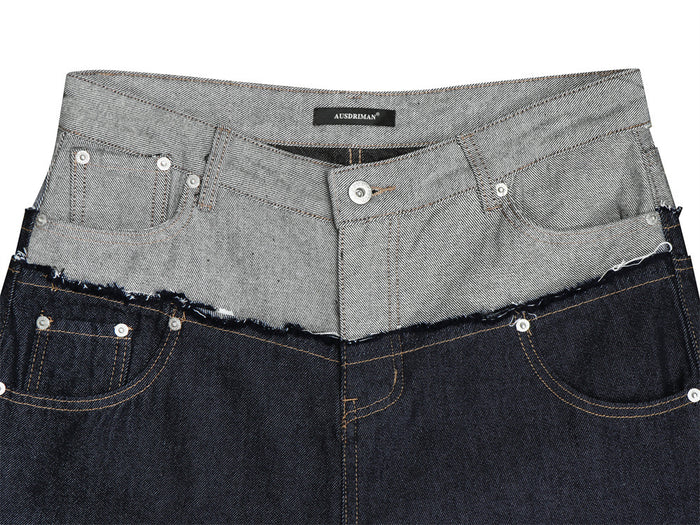 Close-up of the gray double waistband, frayed contrast seam, button fly, and front pockets on dark jeans