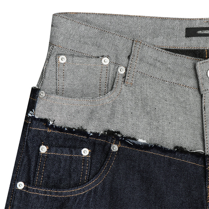 Close-up of layered gray and dark denim waistbands with frayed edging, rivets, and front pocket stitching