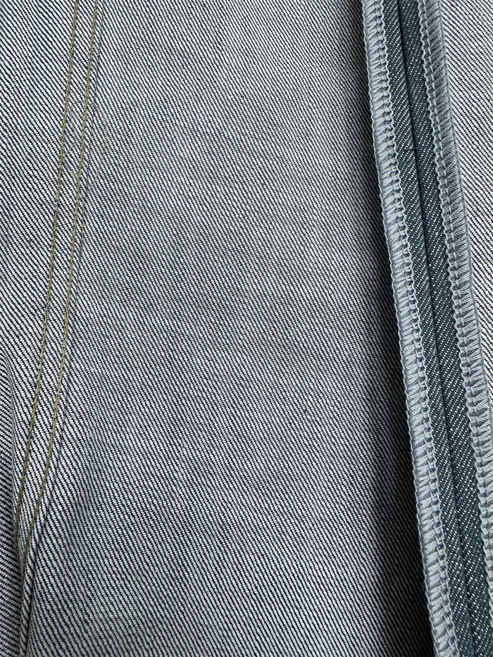 Macro view of lake green denim fabric showing fine diagonal twill texture and stitched seam edge
