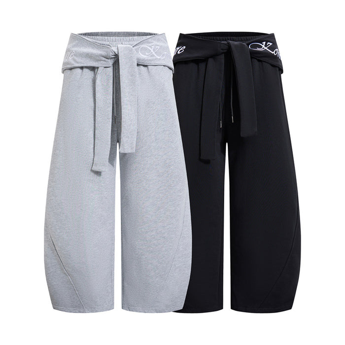 Wide-leg pants shown in light gray and black with fold-over tie waists, white lettering, and relaxed curved legs