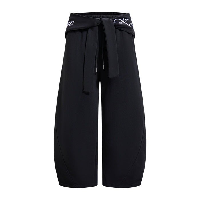 Black wide-leg pants shown from the front with a fold-over tie waistband, white lettering, and curved leg seams