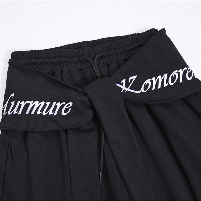 Close-up of black pants showing the folded tie waistband, elastic inner waist, drawstring, and white lettering