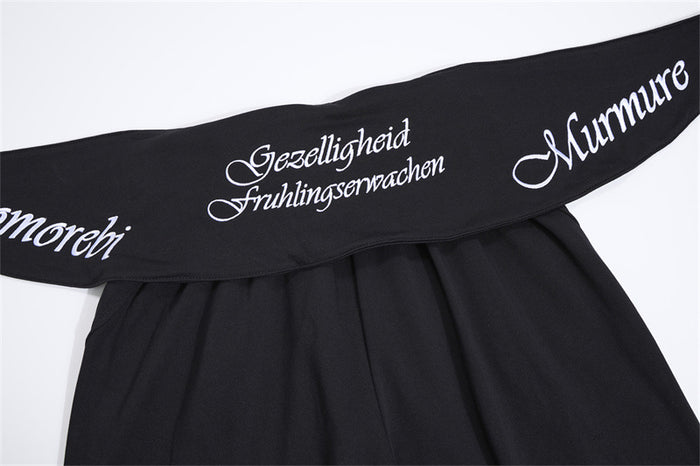 Close-up of a black fold-over waistband with white script embroidery spanning the front of the pants