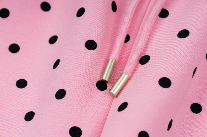 Close-up of pink drawstring ends with metallic gold tips against black polka dot fabric