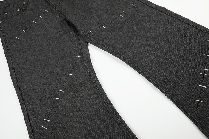 Close-up of black denim legs with diagonal seams, textured weave, and scattered white stitch details