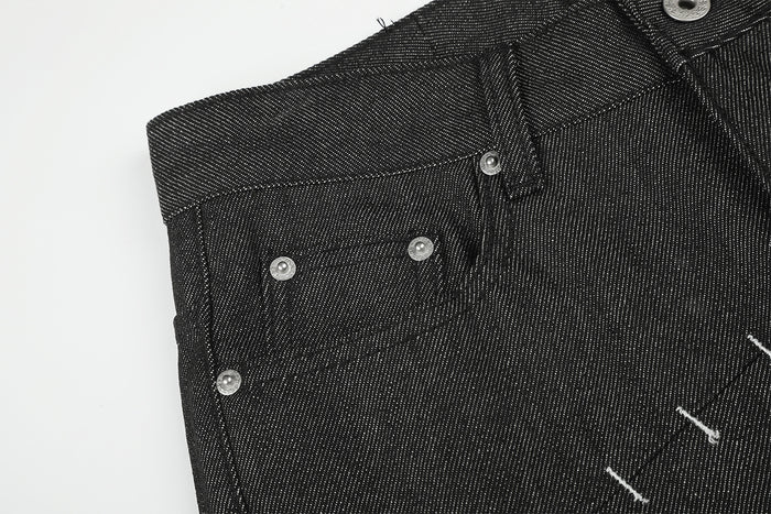 Close-up of the black jeans waistband and front pocket with silver rivets and white stitch accents