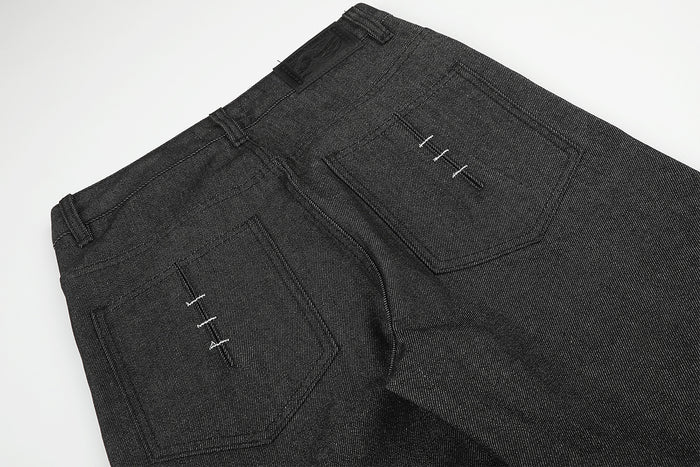 Close-up of a black denim back pocket and curved seam with small white stitch details