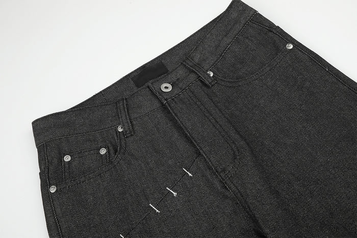 Close-up front view of the black jeans waistband, button closure, pockets, and deconstructed stitching