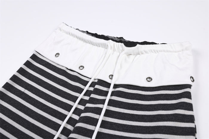 Close-up of black and white striped pants showing the white waistband, metal eyelets, and drawstring
