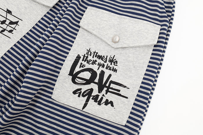 Close-up of a gray cargo pocket with buttoned flap and bold black music-themed lettering on striped pants