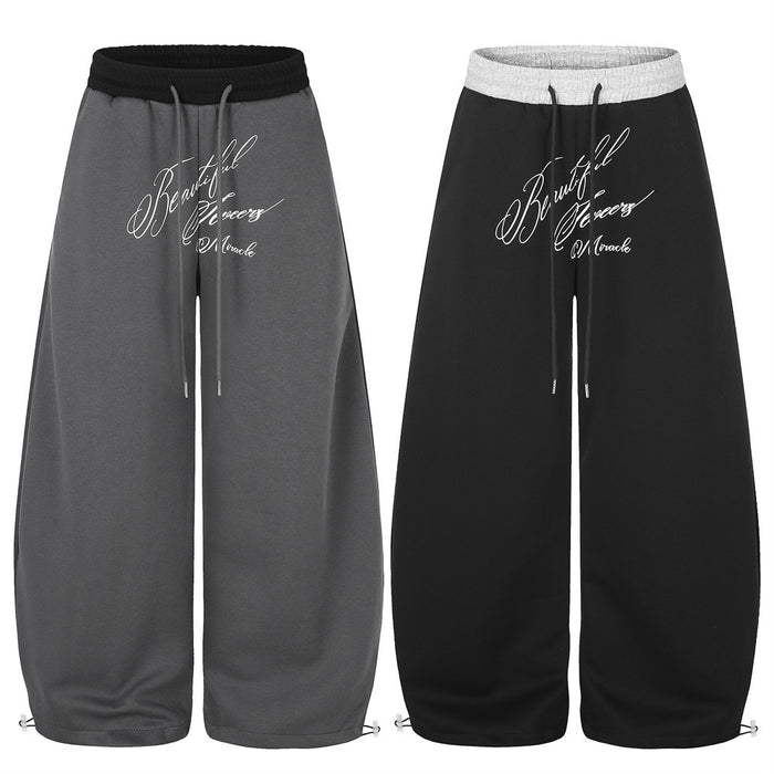 Wide-leg sweatpants in charcoal gray and black with contrasting waistbands, drawcords, and white script prints
