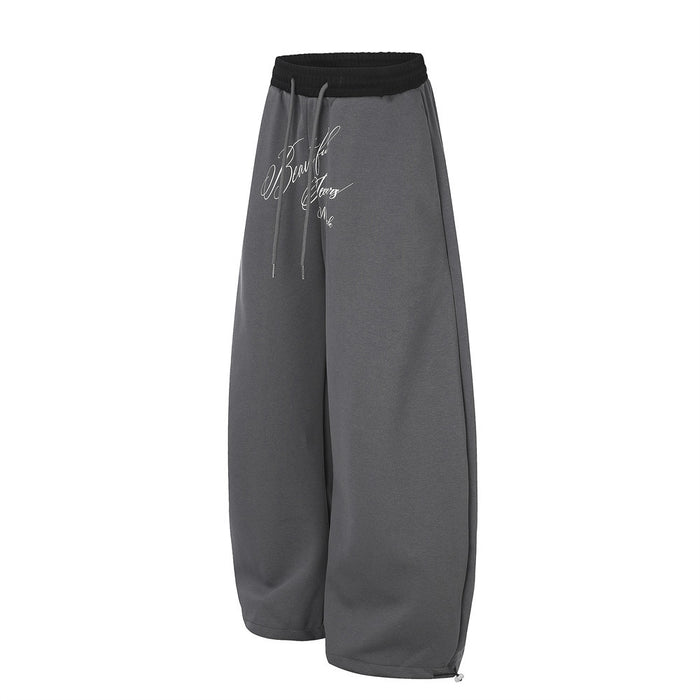 Charcoal gray wide-leg sweatpants shown from an angled side view with a black waistband and front script print
