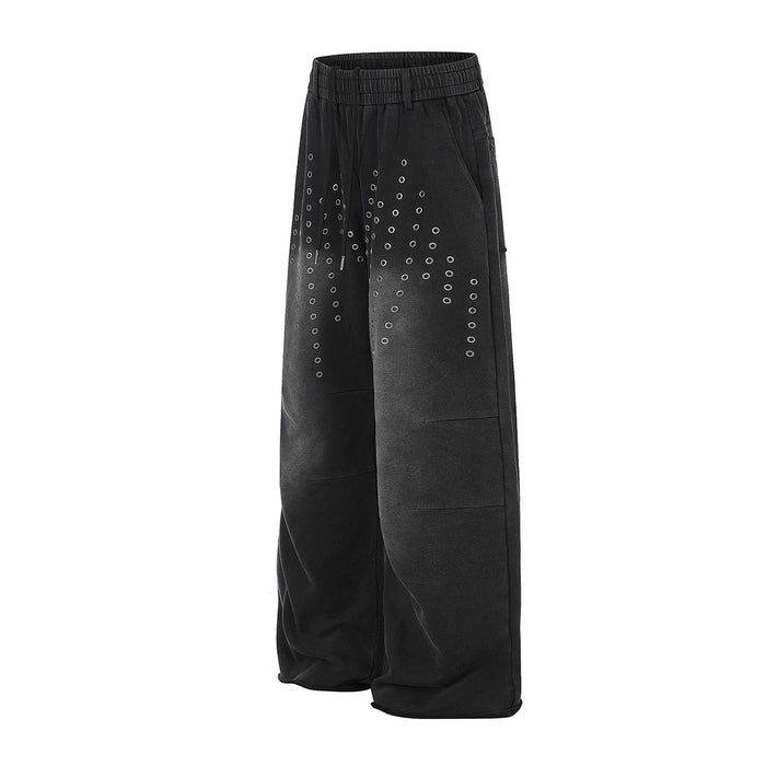 Angled front view of black wide-leg sweatpants featuring rows of silver eyelets across the upper legs