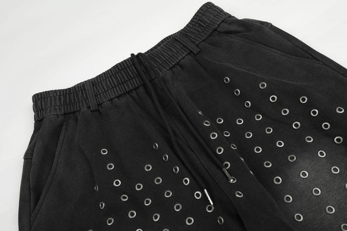 Close-up of the black sweatpants waistband, front seam, and scattered silver eyelets on the upper legs