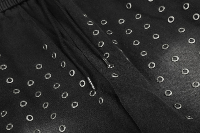 Detailed view of silver eyelets set across black fabric near the center front seam of the sweatpants