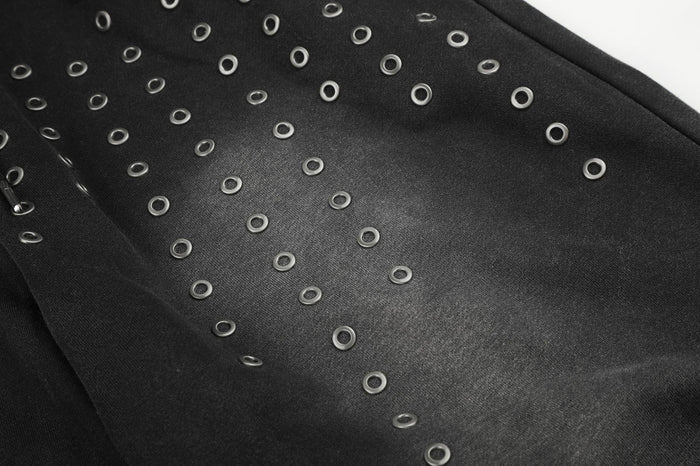 Close-up of silver eyelets scattered across textured black sweatpants fabric beside a stitched panel seam