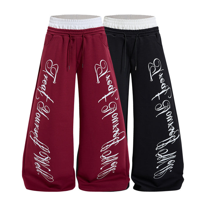 Front view of burgundy and black wide-leg sweatpants with white contrast waistbands, drawstrings, and cursive leg prints