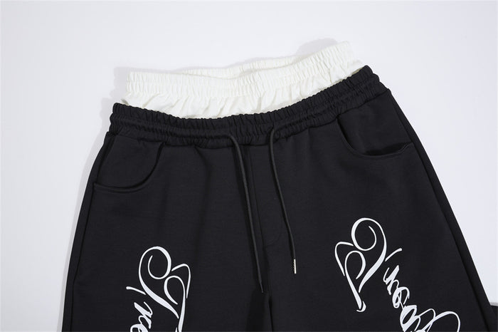 Close-up of black sweatpants showing the white contrast waistband, drawstring, pockets, and partial cursive print