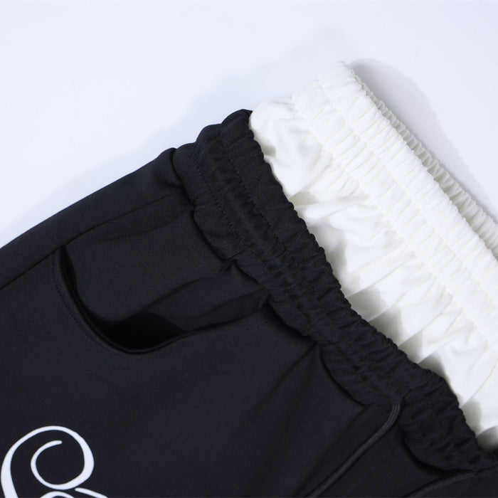 Close-up of black sweatpants pocket and gathered waistband layered over a white contrast waistband