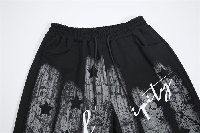 Close-up of black sweatpants showing the elastic drawstring waistband, side pockets, stars, and printed script