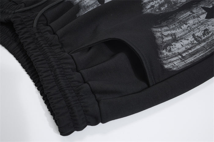 Close-up of black sweatpants showing the elastic waistband, curved side pocket opening, and distressed graphic panel