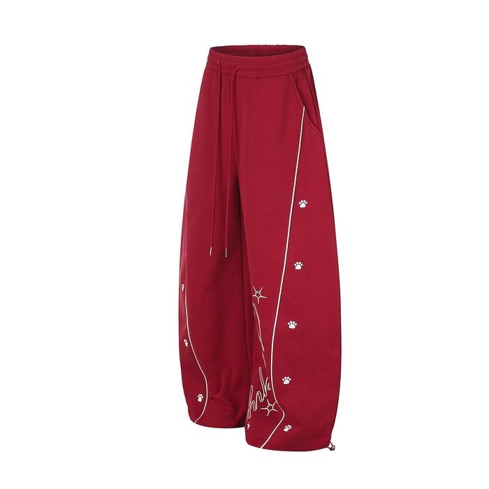 Angled front view of red wide-leg sweatpants with white piping, scattered paw prints, and drawstring waist