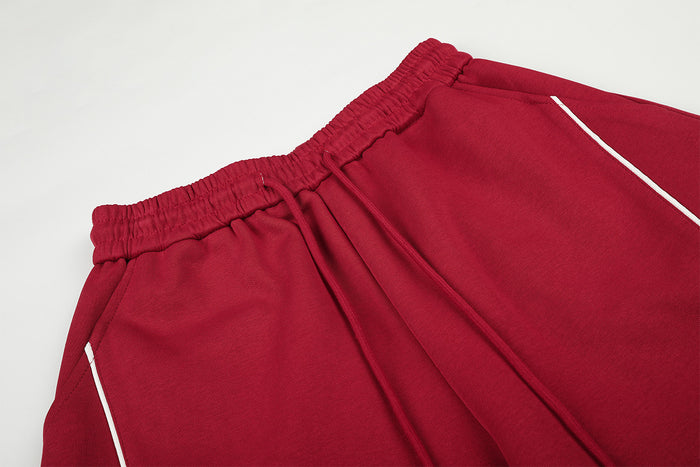 Close-up of the red sweatpants waistband with drawstring, gathered elastic, and white side piping