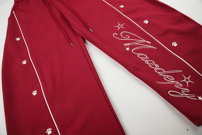 Red sweatpants detail showing white contrast piping, scattered paw prints, drawstrings, and script leg graphic
