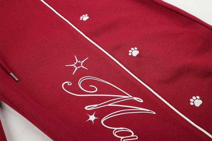 Close-up of white script graphic, star accents, paw prints, and contrast piping on red sweatpants