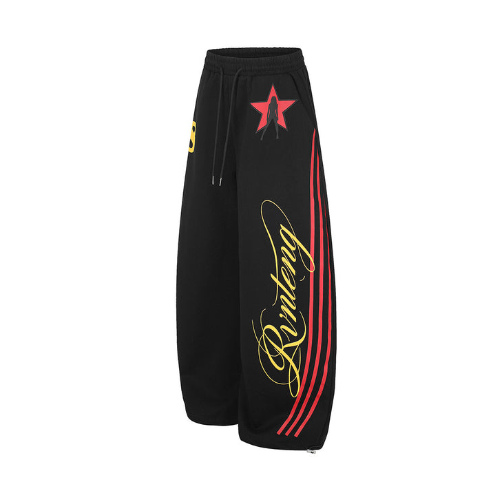 Angled front view of black wide-leg sweatpants highlighting the red star, yellow script, and red side stripes