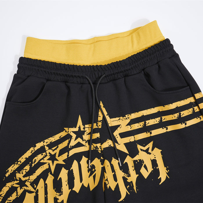Close-up of the black sweatpants waistband with yellow ribbed colorblock band, drawstring, pockets, and star print