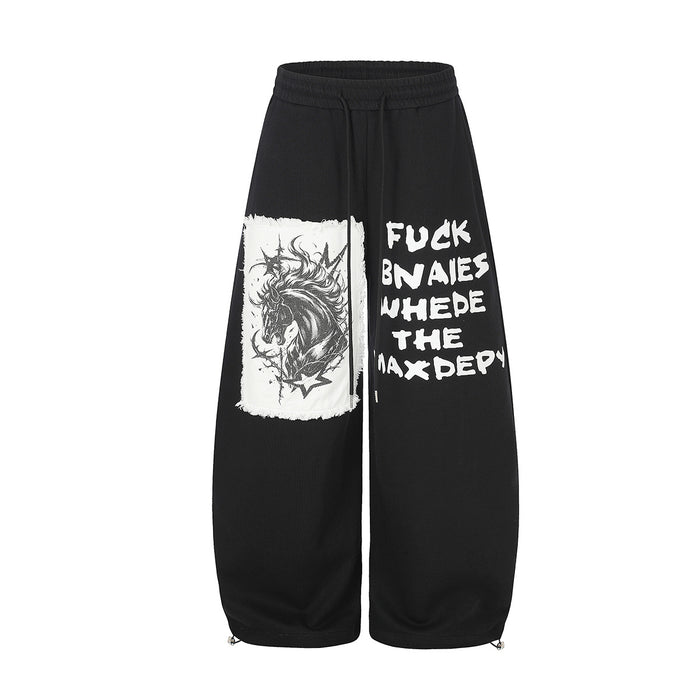 Black wide-leg sweatpants with distressed unicorn appliqué patch and graffiti-style text print on the front leg, shown front
